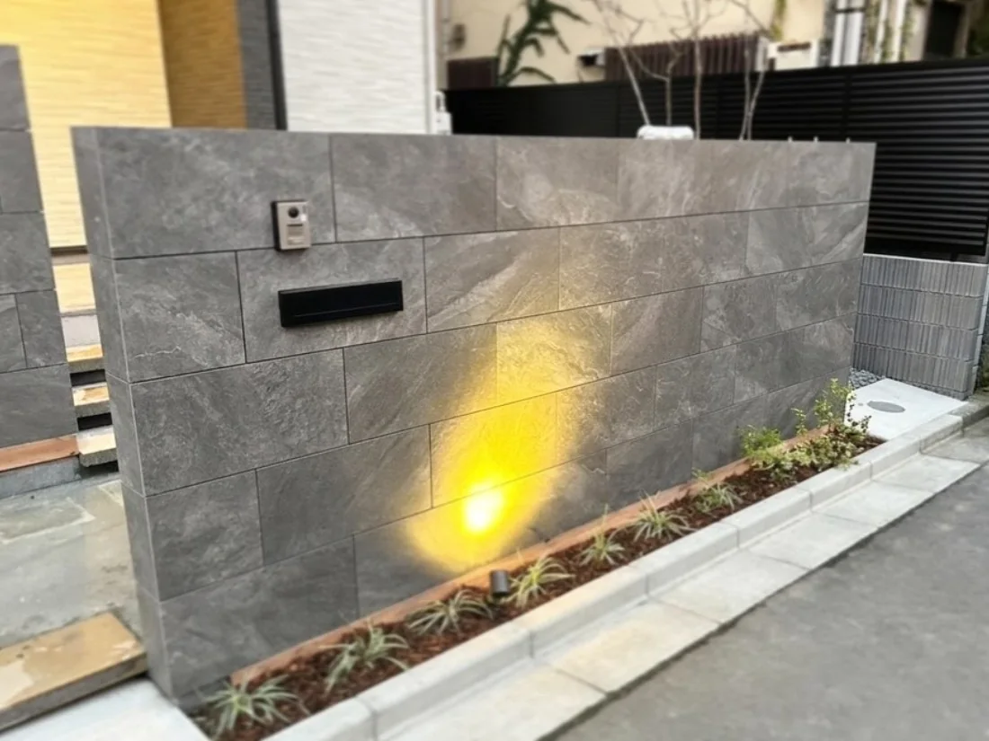 グレーの石調タイルと植栽照明を組み合わせた住宅門塀の施工事例